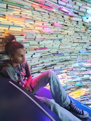 Voorleeskampioen Danischa Bah zit voor een muur van boeken