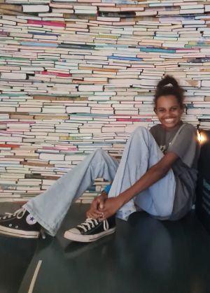 Voorleeskampioen Danischa Bah lacht voor een muur van boeken