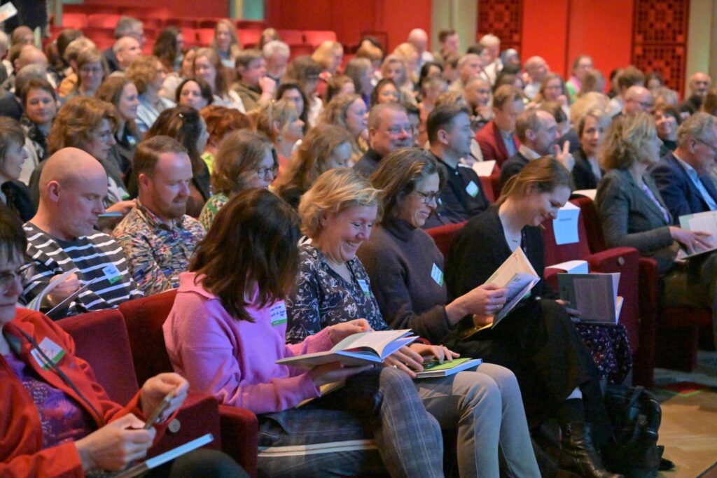 Aanwezigen in de zaal lezen in hun exemplaar van het boek.