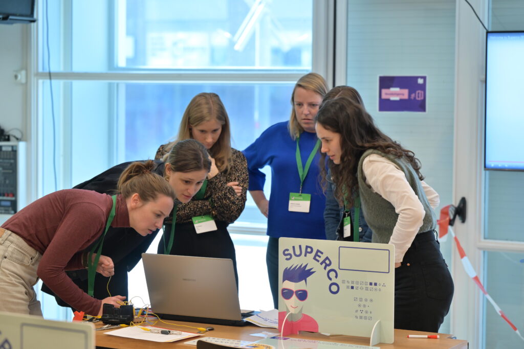 Een team van 6 vrouwen buigt zich tijdens het spel Superco rond een laptop om een opdracht uit te voeren