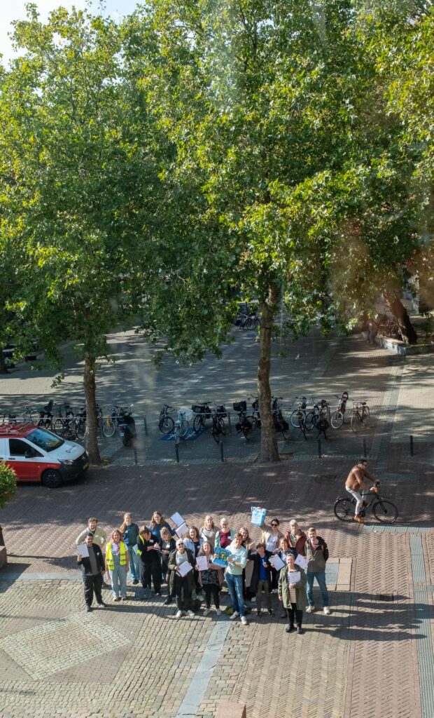 En foto van een groep mensen. De foto is boven gemaakt. De mensen staan op een plein.