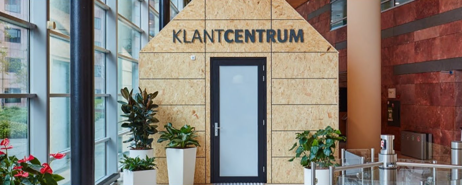 Het klantcentrum: een houten huisje in het UWV-gebouw. Er zit een normale deur in en er staan planten voor het huisje. Op het huisje staat het woord 'Klantcentrum'.