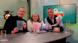Armand, Rosetta en Lodewijk aan tafel in een studio. Ze hebben allemaal een boek vast.